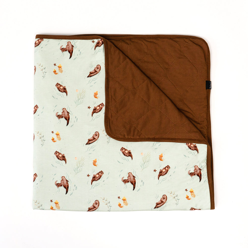 quilted child blanket in otters print, with barrel solid color inside