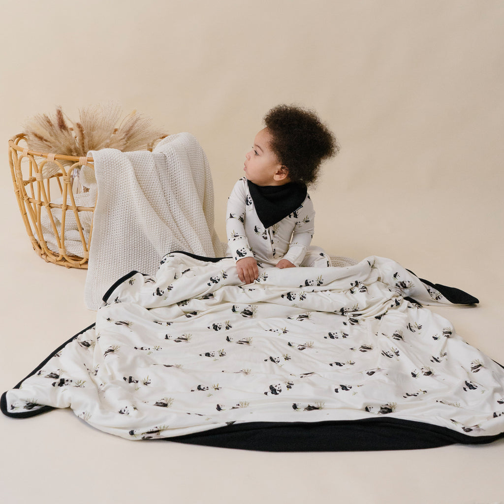 baby wearing panda sleeper, bandana in black and sitting on quilted child blanket in panda