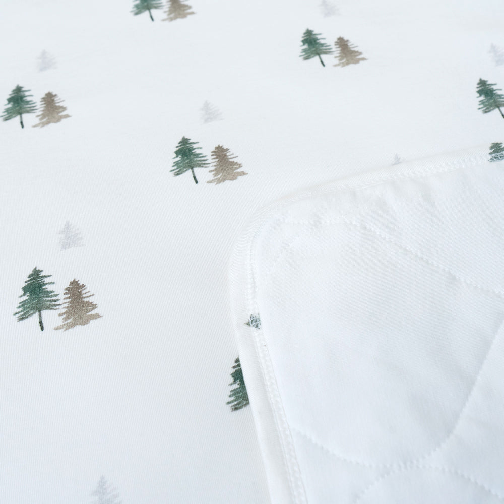quilted child blanket in pine trees print, featuring white background with drawings of green pine trees