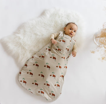 Infant lying comfortably on a white fluffy rug in a cozy bear-print sleep sack