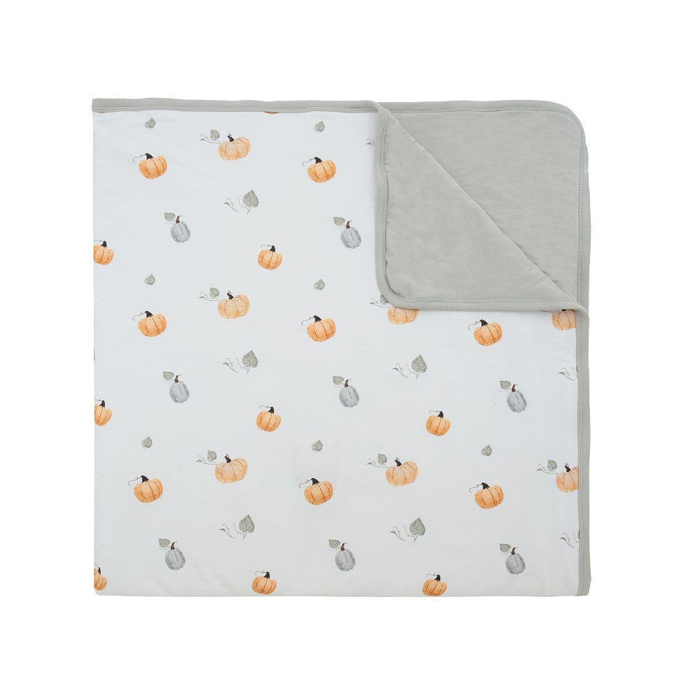 quilted child blanket in pumpkin print, featuring white background with drawings of pumpkins and light green color on the inside